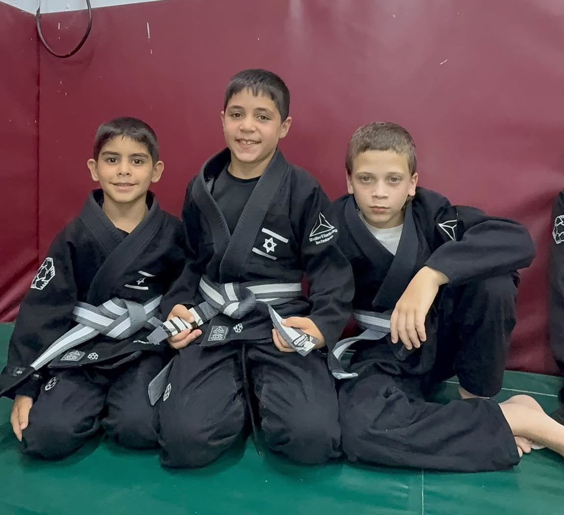 שלושה מתאמנים צעירים ב-Fusion BJJ חיפה עם החגורות החדשות שלהם
